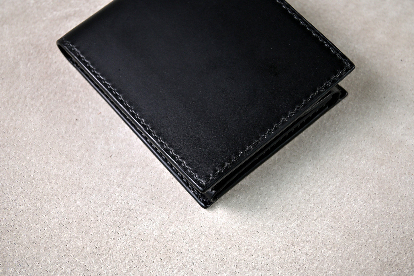 手縫いで仕立てたブッテーロのブラックの二つ折り財布を平置きし、上からステッチの様子を撮影(グレー背景)