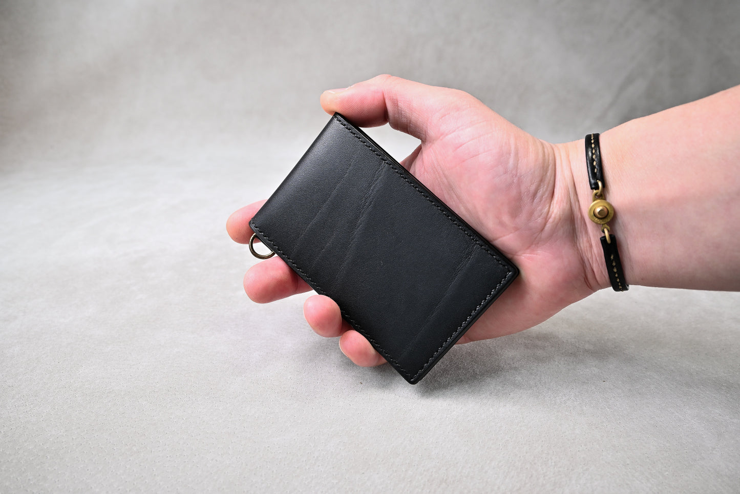 ブッテーロブラックのパスケースを手に持った状態で撮影(コンパクトなサイズ感、Dカン付き)