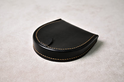 手縫いで仕立てた馬蹄型コインケース「shihu」を平置きで斜めから撮影（ブラックの外装、丸みある立体構造）