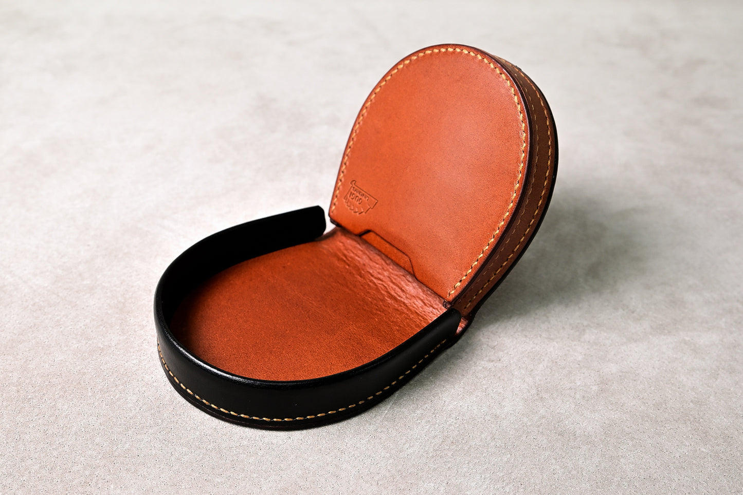 手縫いで仕立てた馬蹄型コインケース「shihu」を平置きで斜めから撮影（ブラックの外装、丸みある立体構造）