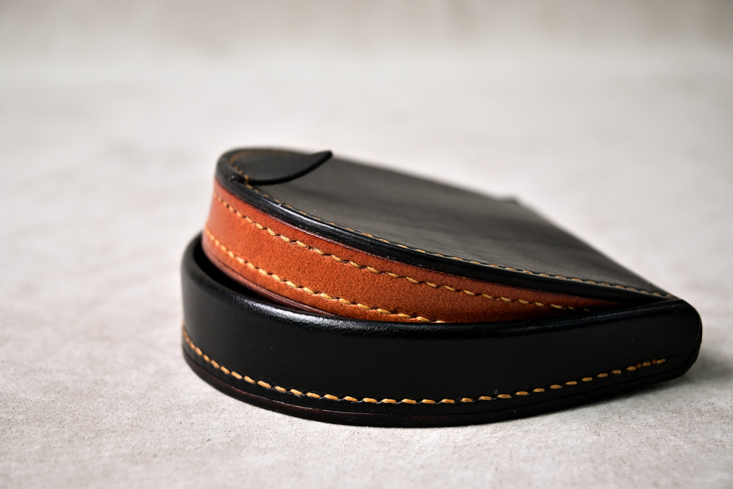 馬蹄型コインケース「shihu」のコバ部分を接写（ブラック外装とキャメル内装の層構造、丁寧なコバ仕上げが見える）