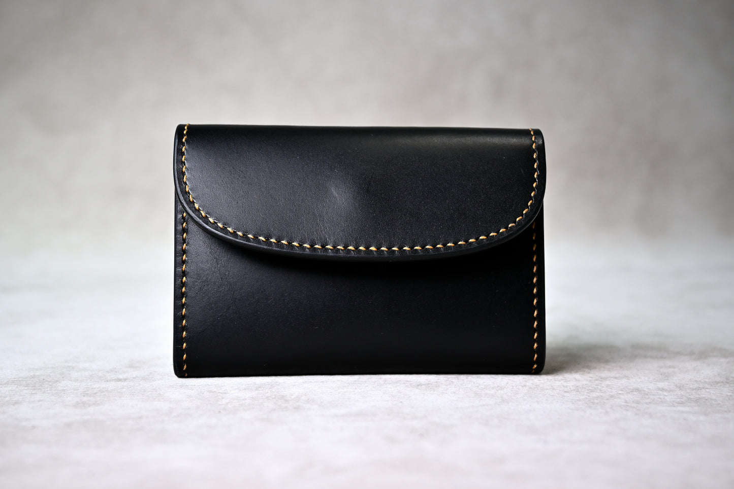 ブッテーロのブラックとキャメルで仕立てたホック留めコインケースを正面から撮影（手縫い、麦色ステッチ）