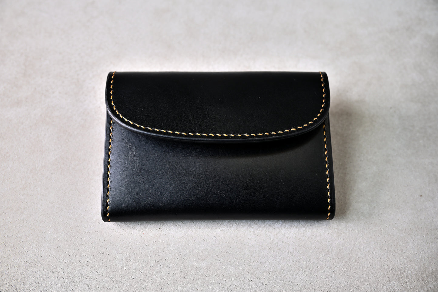 ホック留めのコインケースを真上から撮影（精緻な縫製ラインとシンメトリーな仕立て、手縫い）