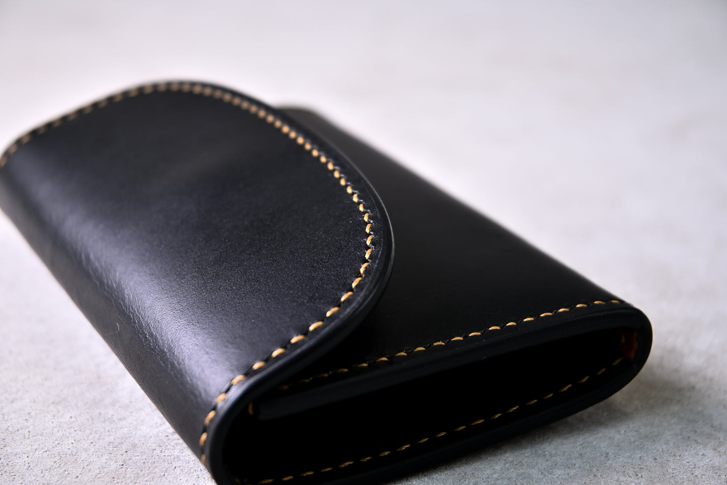 フラップのカーブと縫製ラインを斜めから接写（麦色のステッチが立体的に映える構図）