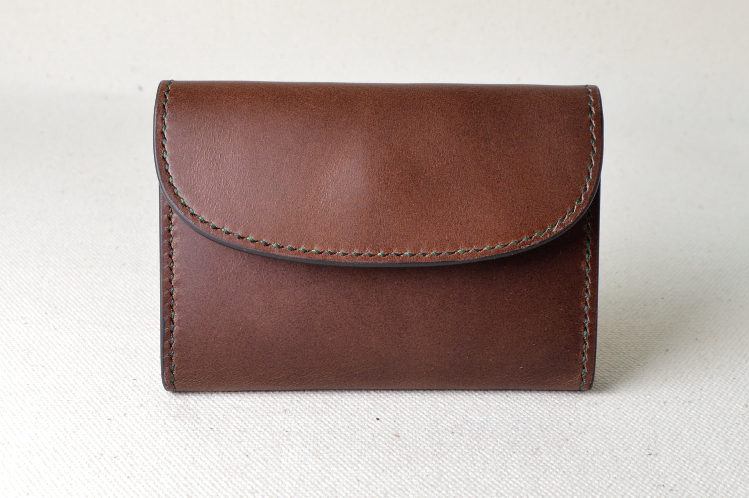 ブッテーロのブラウンとグリーンで仕立てたTetoコインケースを正面から撮影（手縫い、クラシックな配色）