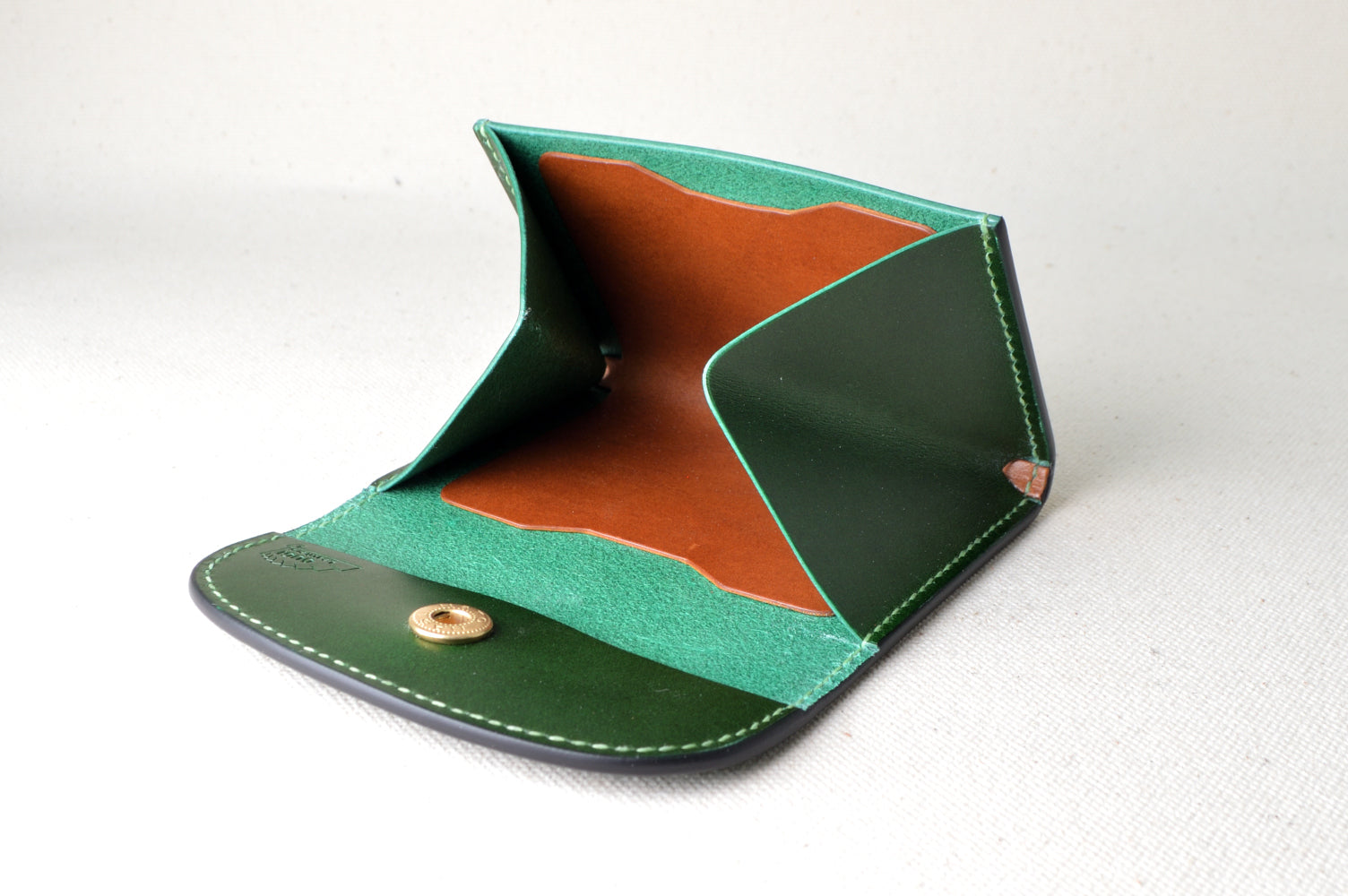 外装グリーン、内装キャメルのホック式コインケースを開いた状態で撮影（ライトグリーンのステッチが映える、仕切り付き）