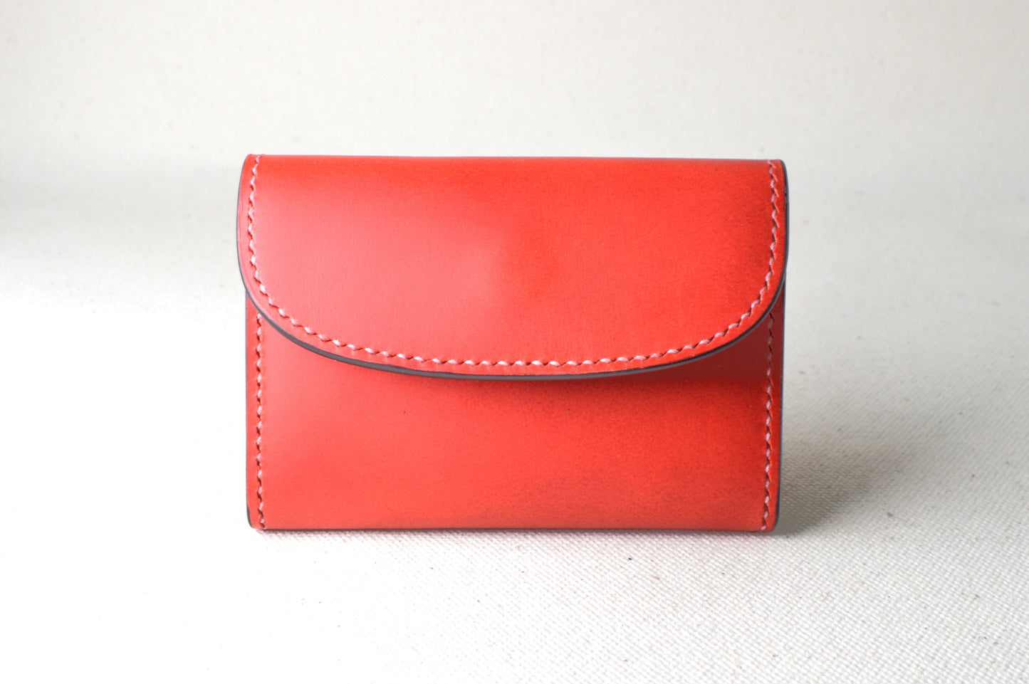 ブッテーロのレッド外装にブラックとピンクの内装を合わせたTetoコインケースを正面から撮影（華やかな配色、手縫い）