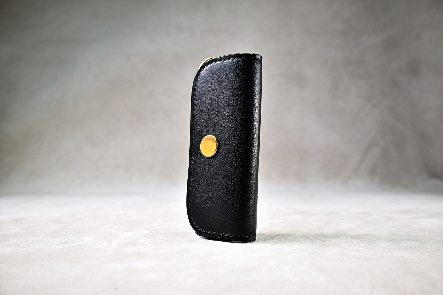 ブッテーロのブラックで仕立てたキーケースを立てかけて撮影（真鍮ホック、シンプルな外装）