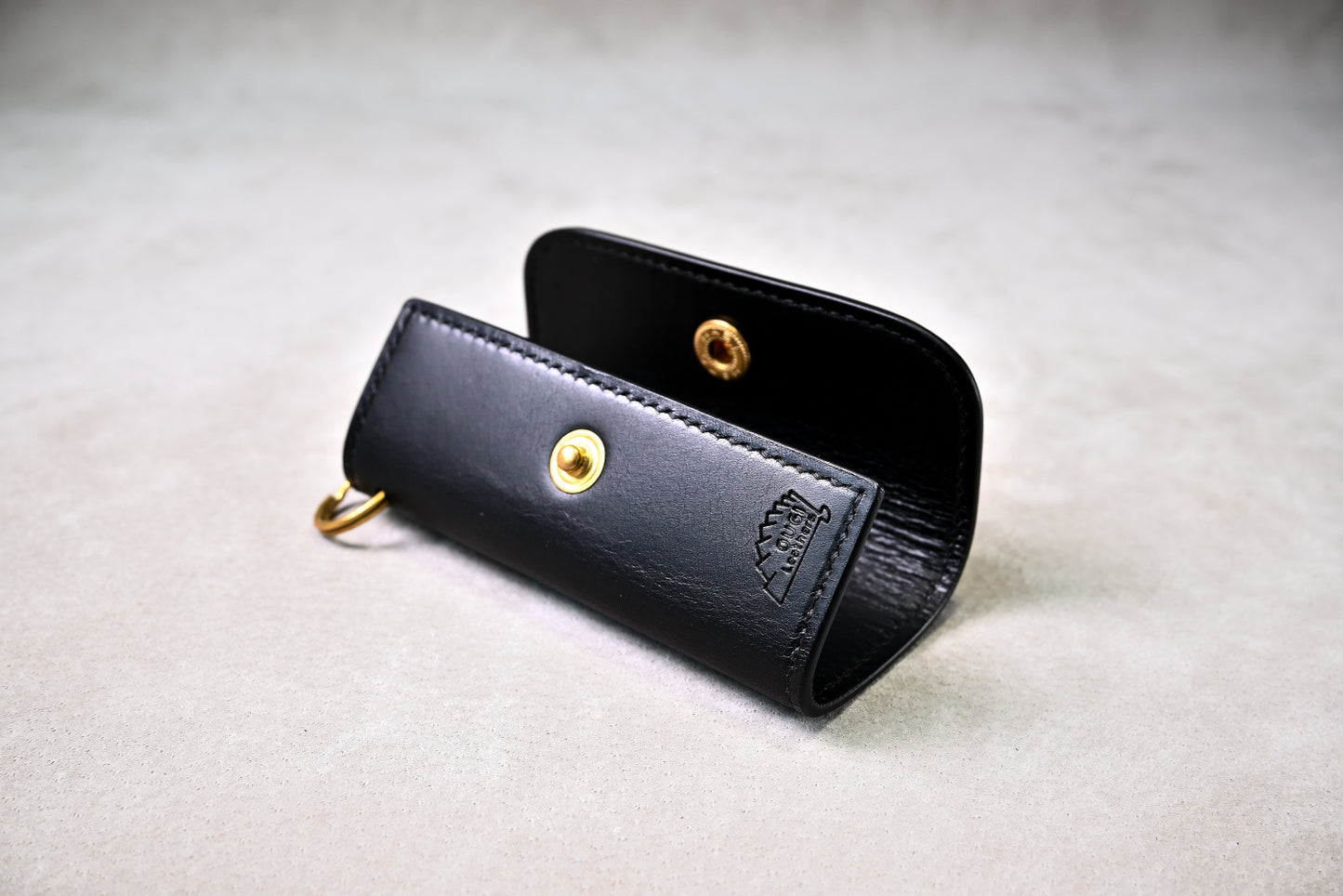 開いた状態でブランドロゴが見えるキーケースを斜めから撮影（真鍮ホック、手縫い）